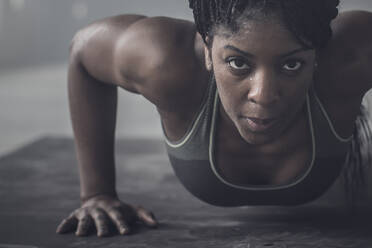 Black woman doing push-ups in dark gym - BLEF08160