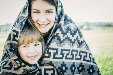 Caucasian sisters wrapped in blanket on farm - BLEF08182