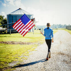 Kaukasisches Mädchen winkt mit amerikanischer Flagge auf einem Bauernhof - BLEF08190