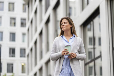 Young businesswoman with coffee to go cup, office building in the background - DIGF07086