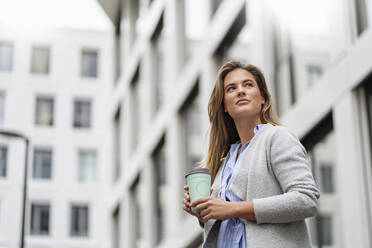 Young businesswoman with coffee to go cup, office building in the background - DIGF07087