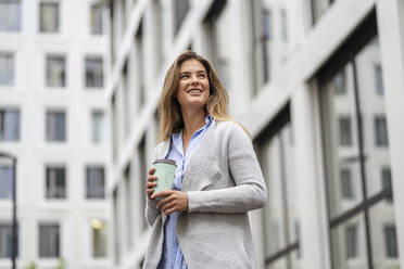 Junge Geschäftsfrau mit Coffee-to-go-Becher, Bürogebäude im Hintergrund - DIGF07088