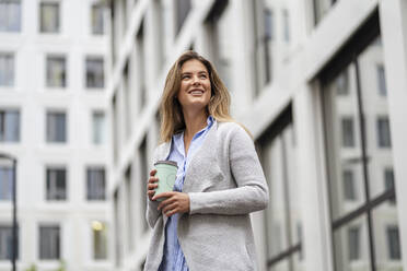 Young businesswoman with coffee to go cup, office building in the background - DIGF07088