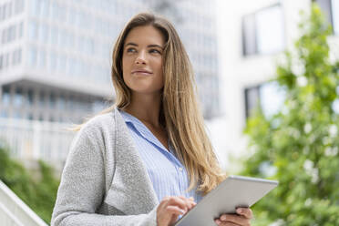 Portrait of young businesswoman using tablet, office buildings in the background - DIGF07096