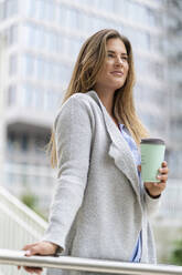 Junge Geschäftsfrau mit Coffee-to-go-Becher, Bürogebäude im Hintergrund - DIGF07098