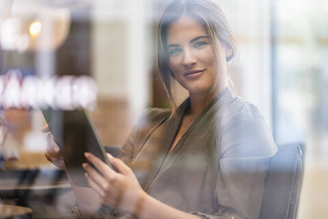 Junge Geschäftsfrau mit Tablet in einem Café, durch ein Fenster gesehen, lizenzfreies Stockfoto