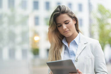 Portrait of young businesswoman using tablet, office buildings in the background - DIGF07125