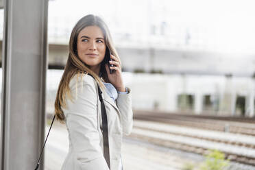 Junge Geschäftsfrau mit Smartphone, stehend auf dem Bahnhof - DIGF07143
