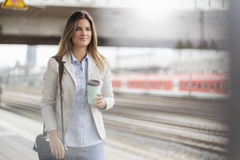 Junge Geschäftsfrau mit Coffee-to-go-Becher, stehend am Bahnhof, lizenzfreies Stockfoto