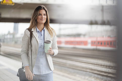 Junge Geschäftsfrau mit Coffee-to-go-Becher, stehend am Bahnhof - DIGF07144