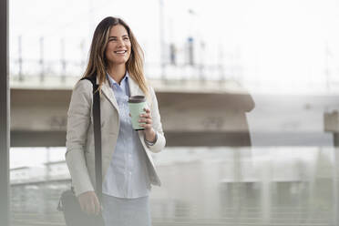 Junge Geschäftsfrau mit Coffee-to-go-Becher, stehend am Bahnhof - DIGF07145