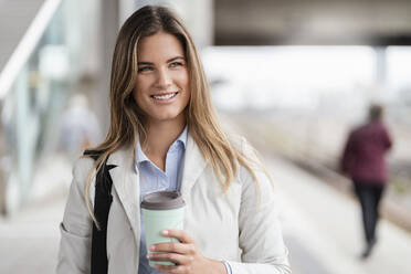 Junge Geschäftsfrau mit Coffee-to-go-Becher, stehend am Bahnhof - DIGF07146