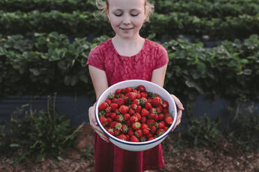 Hoher Winkel Blick auf lächelnde Mädchen mit frischen Erdbeeren in Schüssel gegen Pflanzen - OGF00002