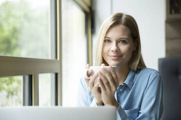 Businesswoman with cup of coffee, in front of laptop - MFRF01331