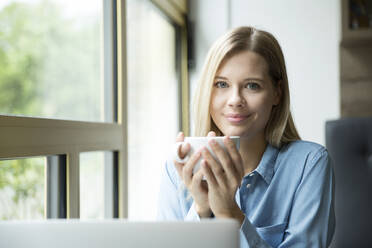 Geschäftsfrau mit einer Tasse Kaffee, vor einem Laptop - MFRF01331