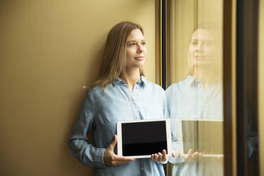Businesswoman holding tablet looking out of window - MFRF01332