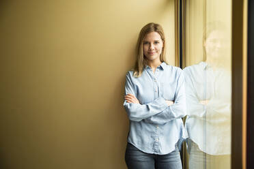 Businesswoman standing on a window, looking on camera, ams crossed - MFRF01337