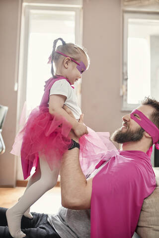 Vater und Tochter spielen Superheld und Superfrau und tun so, als würden sie fliegen, lizenzfreies Stockfoto