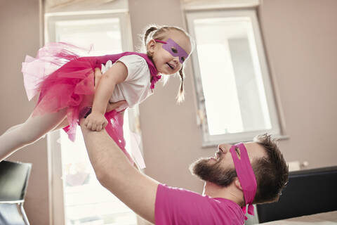 Vater und Tochter spielen Superheld und Superfrau und tun so, als würden sie fliegen, lizenzfreies Stockfoto