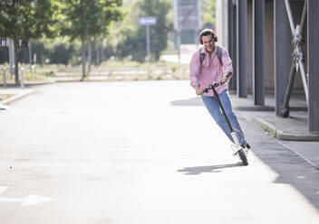 Businessman with headphones and backpack riding his E-Scooter - UUF18164