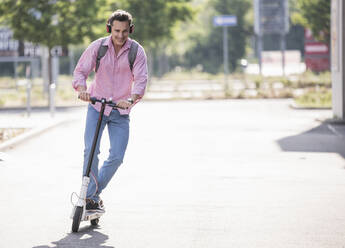 Businessman with headphones and backpack riding his E-Scooter - UUF18165