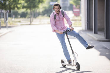 Businessman with headphones and backpack riding his E-Scooter - UUF18166