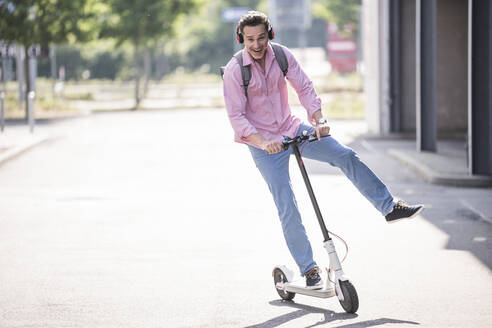 Geschäftsmann mit Kopfhörern und Rucksack auf seinem E-Scooter - UUF18166