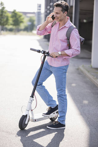 Businessman using smartphone, standing on E-Scooter stock photo