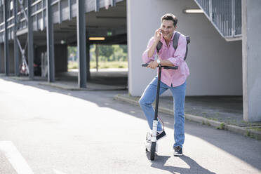 Geschäftsmann mit Smartphone, stehend auf E-Scooter - UUF18173