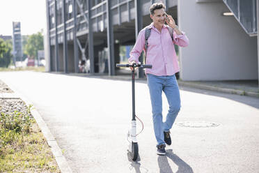 Businessman using smartphone, pushing his E-Scooter - UUF18174