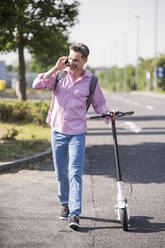 Businessman using smartphone, pushing his E-Scooter - UUF18175