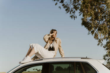 Weiblicher Reisender auf weißem Autodach sitzend - ERRF01602