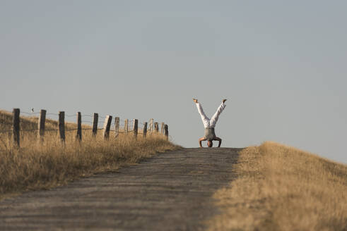 Mid distance view of mature man doing headstand on road against clear sky - KJF00319