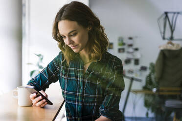 Young woman sitting in coffee shop, using smartphone - JOSF03317