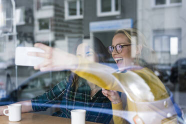 Zwei Freundinnen sitzen in einem Café und machen Smartphone-Selfies - JOSF03320