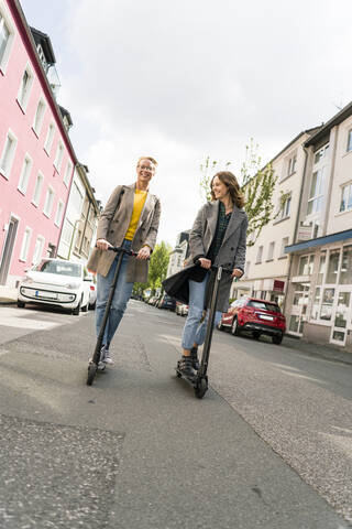 Junge Frauen fahren auf Elektrorollern auf der Straße, lizenzfreies Stockfoto