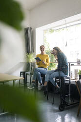 Freunde sitzen in einem Café, benutzen ein digitales Tablet, ein E-Scooter lehnt auf dem Tisch - JOSF03323