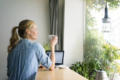Blonde Frau sitzt in einem Café, benutzt einen Laptop und trinkt Kaffee - JOSF03343