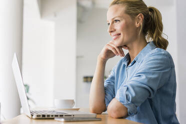 Blonde Frau sitzt in einem Café und benutzt einen Laptop - JOSF03345