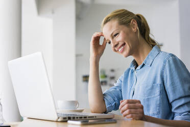 Blonde Frau sitzt in einem Café und benutzt einen Laptop - JOSF03346