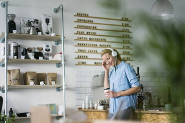 Young woman listening music, wearing headphones, standing in coffee shop - JOSF03350