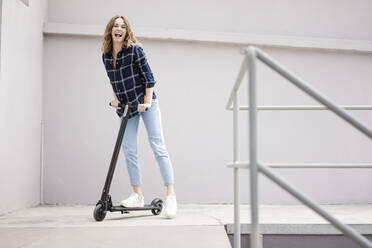 Junge Frau mit Elektroroller in einem Loft - JOSF03360