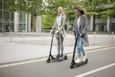 Young women riding electric scooters in the street - JOSF03378