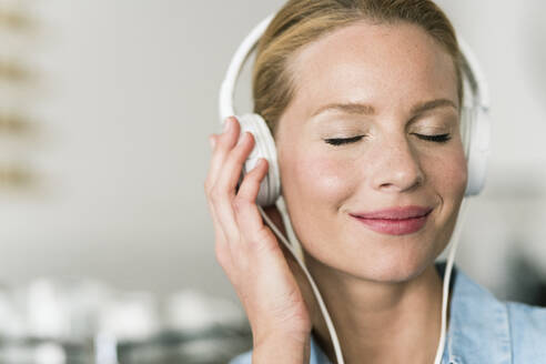 Blonde Frau in einem Café mit Kopfhörern, die Musik hören - JOSF03385