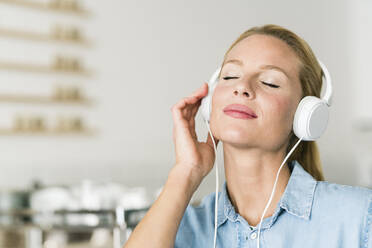 Blonde Frau in einem Café mit Kopfhörern, die Musik hören - JOSF03386
