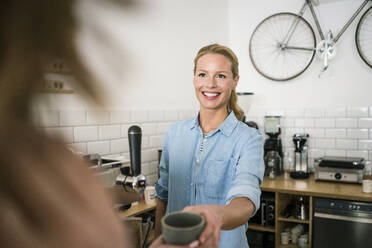 Junge Geschäftsinhaberin in ihrem Café, die einem Kunden Kaffee serviert - JOSF03389