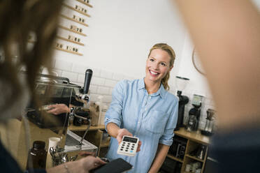Junge Geschäftsinhaberin in ihrem Café, die ein Kartenlesegerät für kontaktloses Bezahlen in der Hand hält - JOSF03390