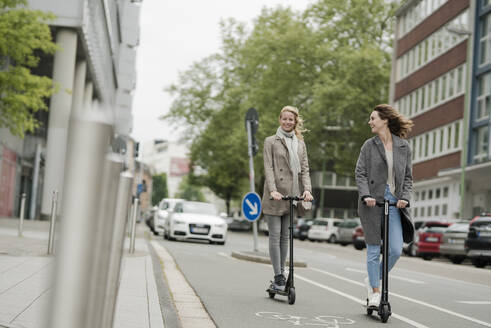 Junge Frauen fahren auf Elektrorollern auf der Straße - JOSF03403