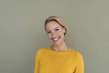 Porträt einer lächelnden blonden Frau, die einen gelben Pullover trägt - JOSF03405