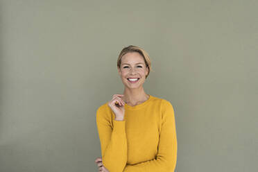 Porträt einer lächelnden blonden Frau, die einen gelben Pullover trägt - JOSF03406